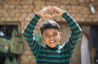 A boy in India makes a heart gesture with his hands