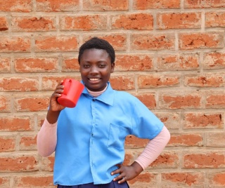 Mary, a school pupil from Zambia smiles while she enjoys a mug of porridge served by Mary's Meals volunteers.