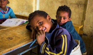 A young boy rests against a table in class