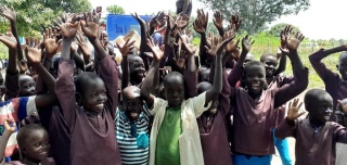 Children smiling and waving their hands in the air while standing outside.